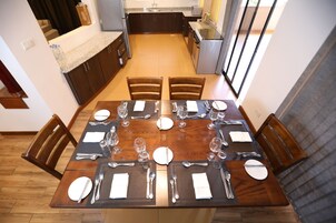 Comedor con mesa de madera preparada para seis personas, rodeado de sillas, en una cocina moderna con vista al área de estar.