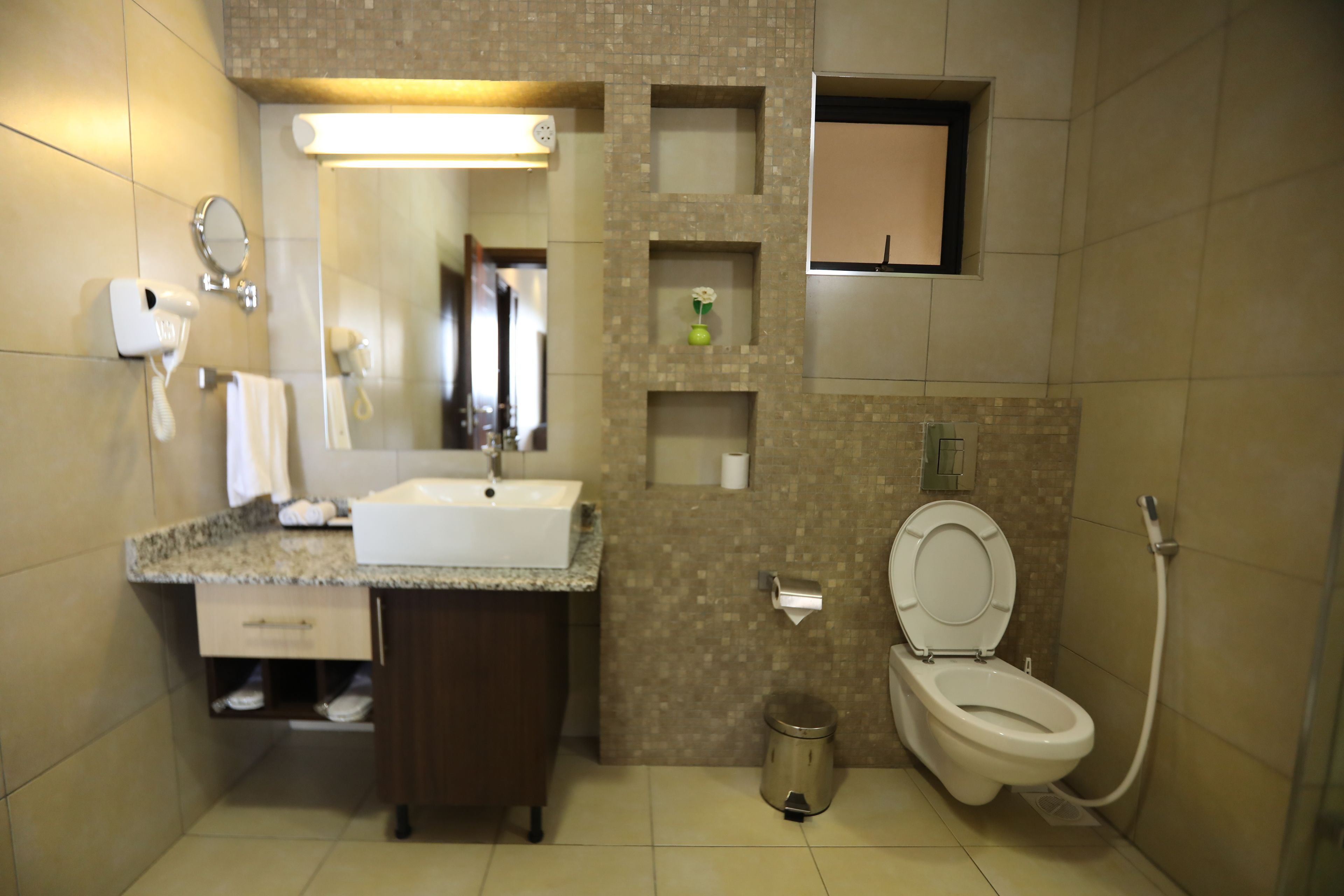 A bathroom with a sink, mirror, toilet, and a trash can.