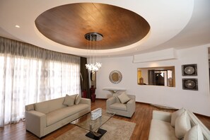 A modern living room with a wooden ceiling, two sofas, a glass coffee table, and decorative wall art. - Bidwood Suite Hotel (Nairobi)