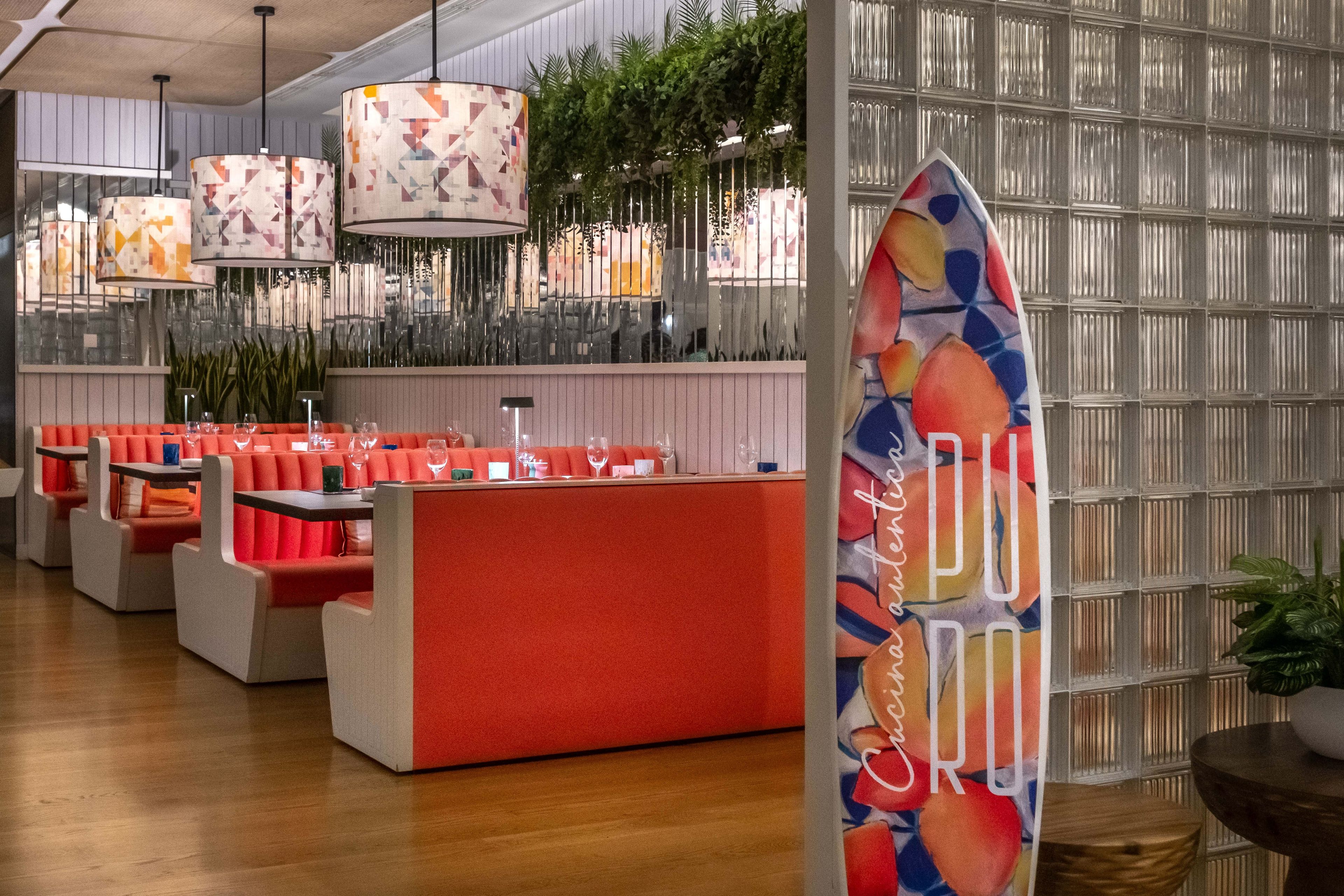 Restaurante moderno com assentos vermelhos, área de bar e luminárias pendentes.