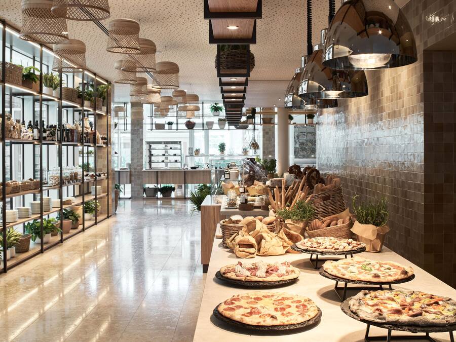Een ruime hotel lobby met een lange receptiebalie, planken met diverse objecten, en meerdere hangende lampen.