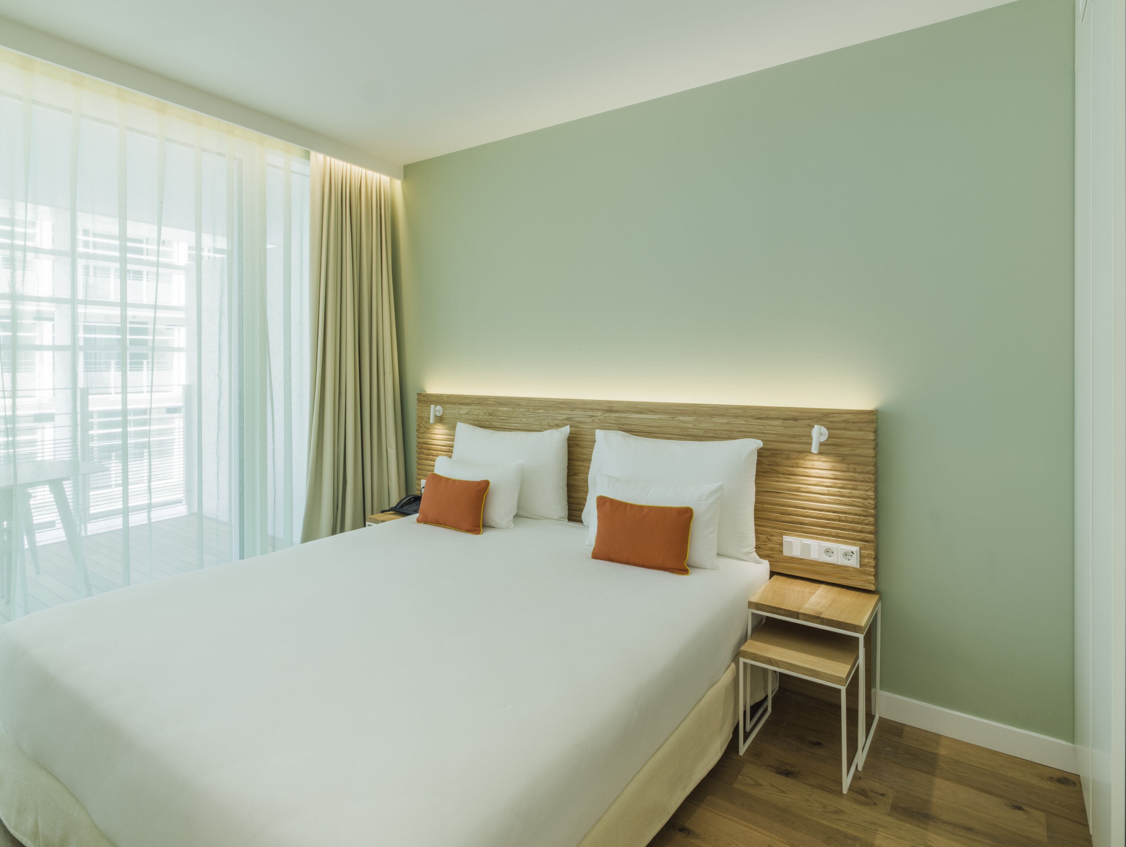 Ein Hotelzimmer mit einem großen Bett, zwei Kissen, einem Nachttisch und einem Fenster mit Vorhängen.