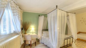 Een slaapkamer met een hemelbed, nachtkastje, stoel en radiator.