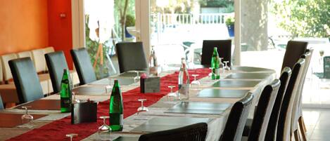 A conference table set with chairs, wine glasses, and bottles, in a room with a view of greenery outside.