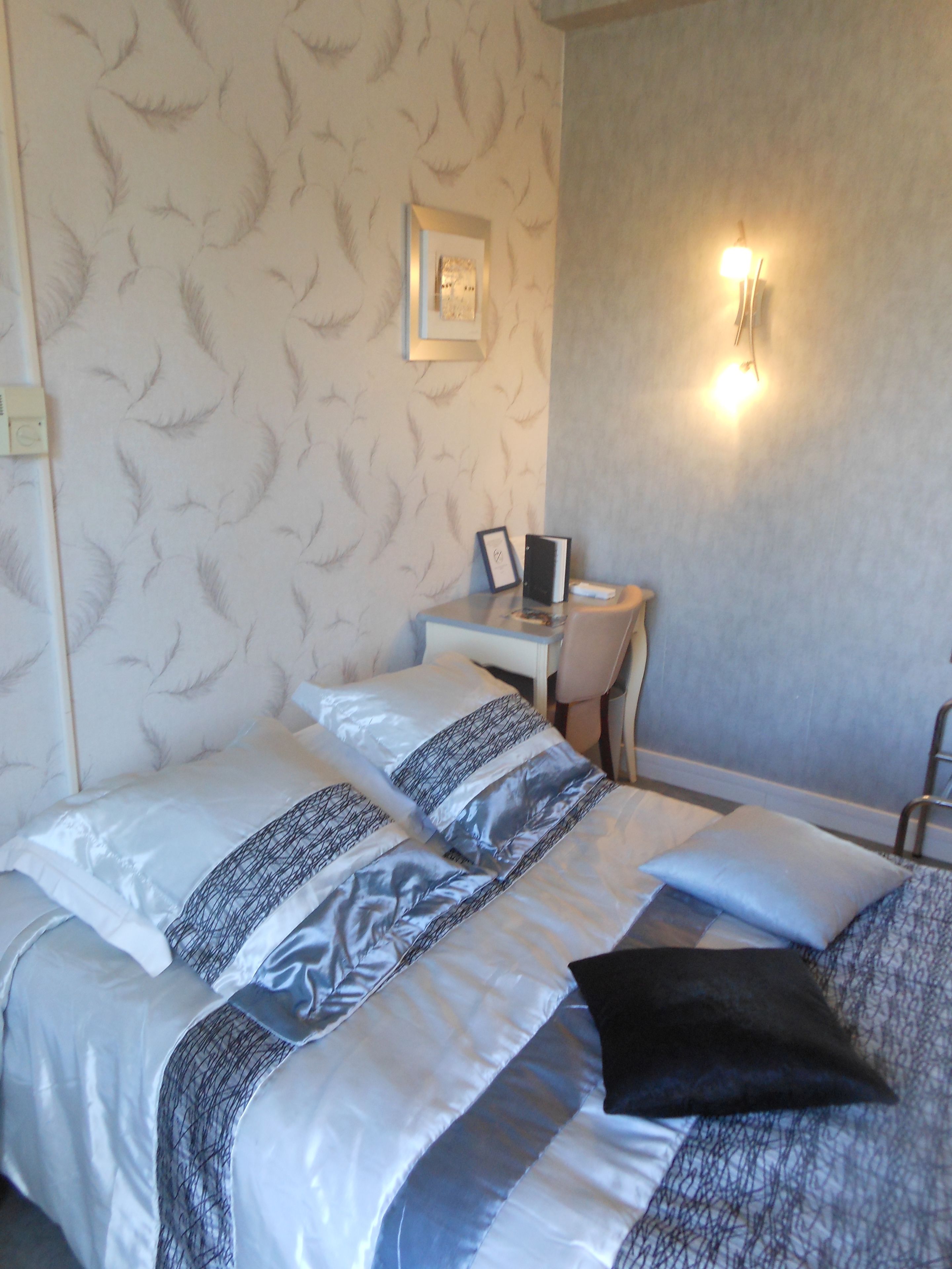 A hotel room with a bed, a desk, and a wall-mounted light.