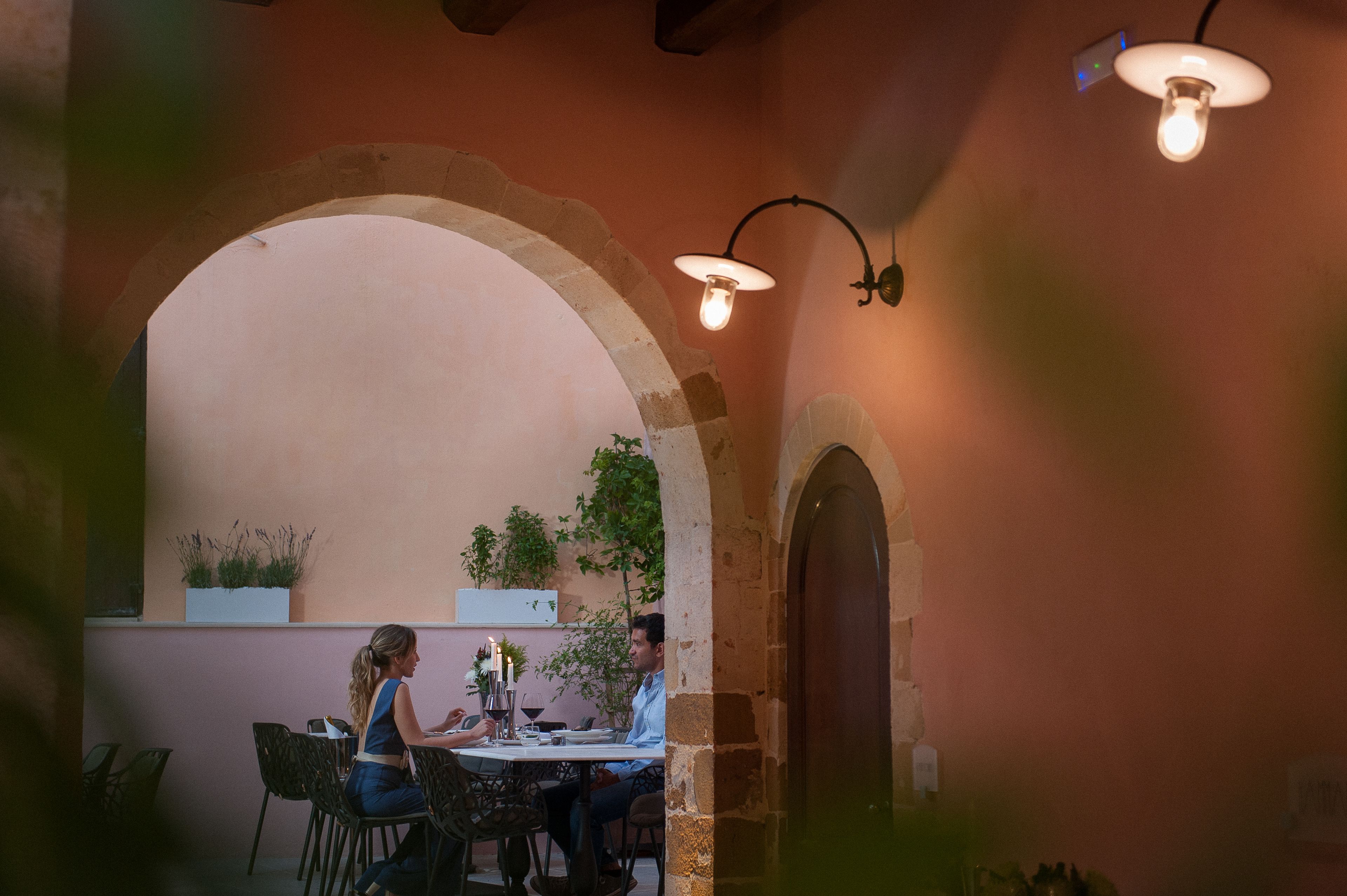 An outdoor dining area with a stone archway, a table set with candles, and a potted plant.