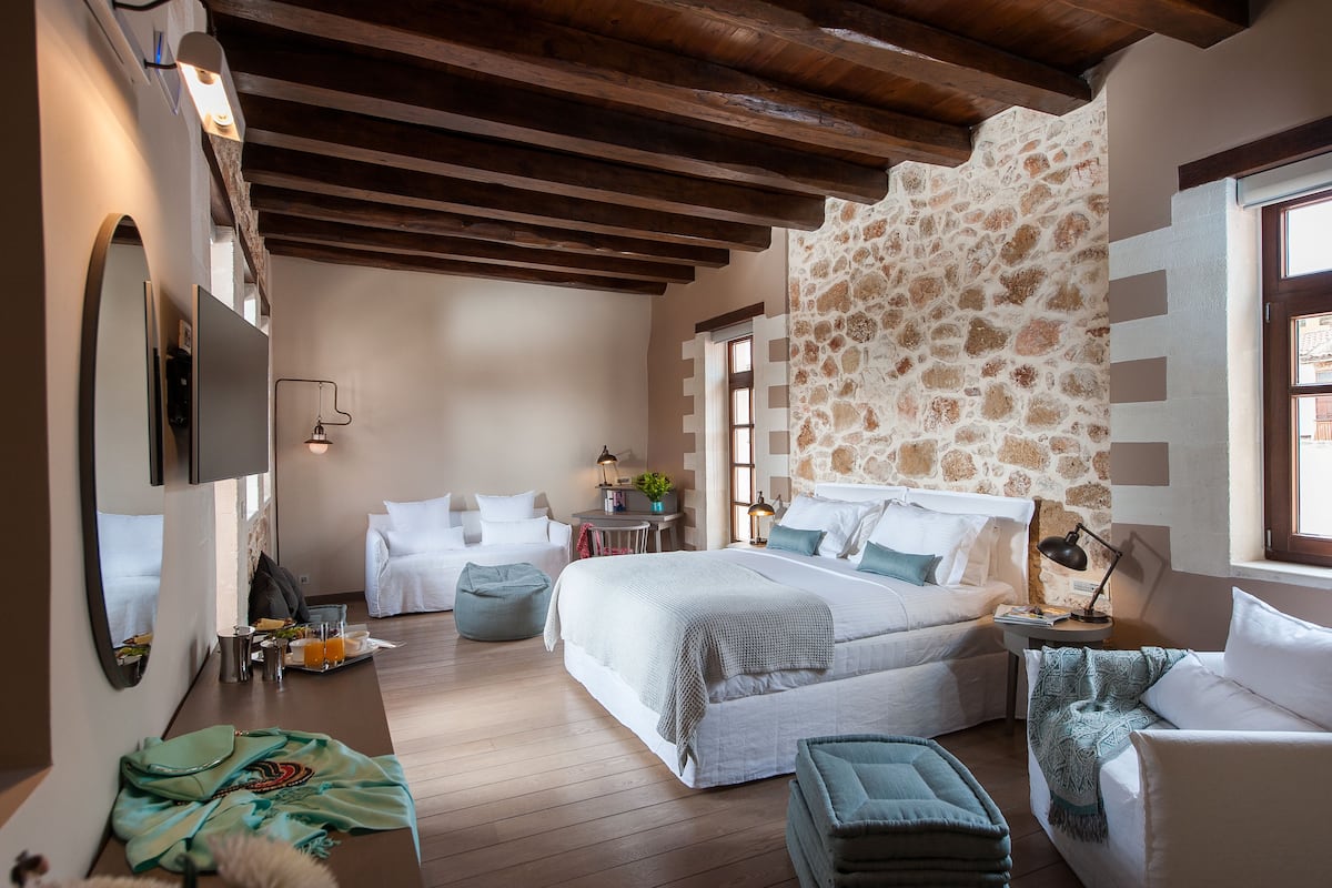 Une chambre avec un mur en pierre, des poutres en bois, un lit, un bureau et une chaise.