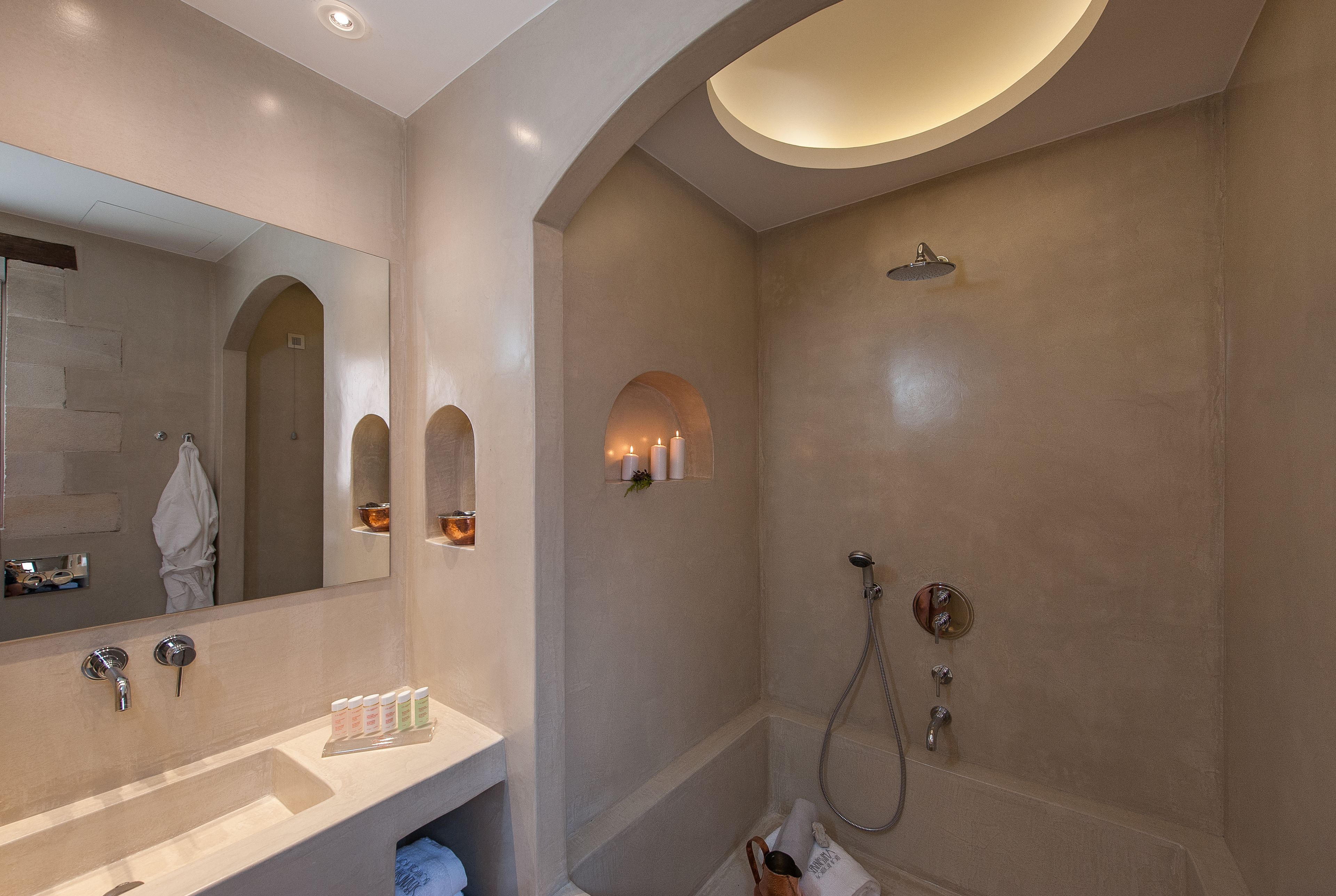 Un baño moderno con un espejo grande, un lavamanos con artículos de aseo y una ducha a ras de suelo con cabezal de ducha manual.