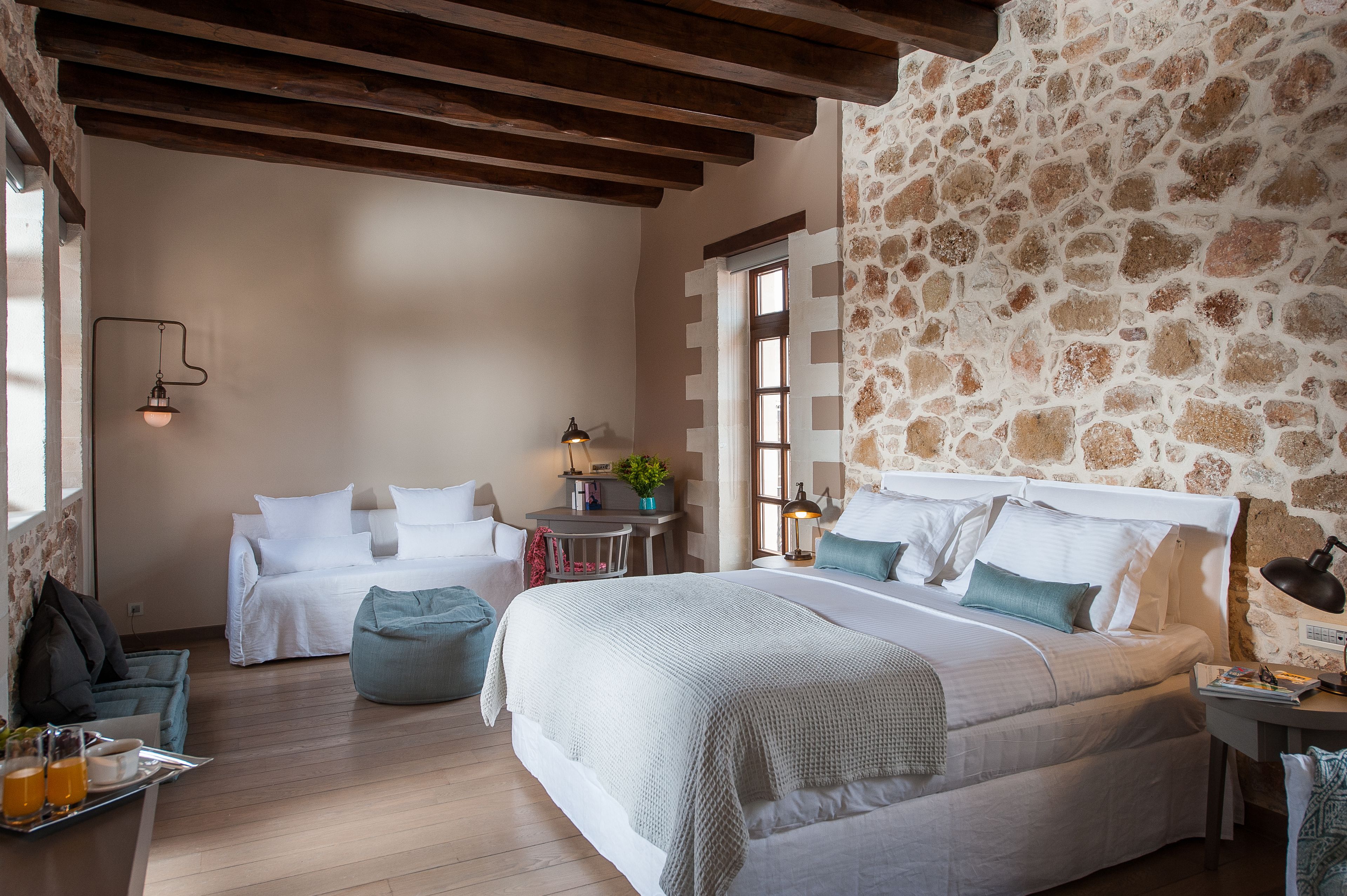 Una camera accogliente con un letto grande, un letto più piccolo, una scrivania e un muro in pietra.