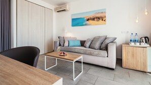 A modern living room with a grey sofa, a wooden coffee table, and a wooden cabinet with water bottles and a kettle. - LABRANDA Alyssa Suite Hotel (Yaiza)