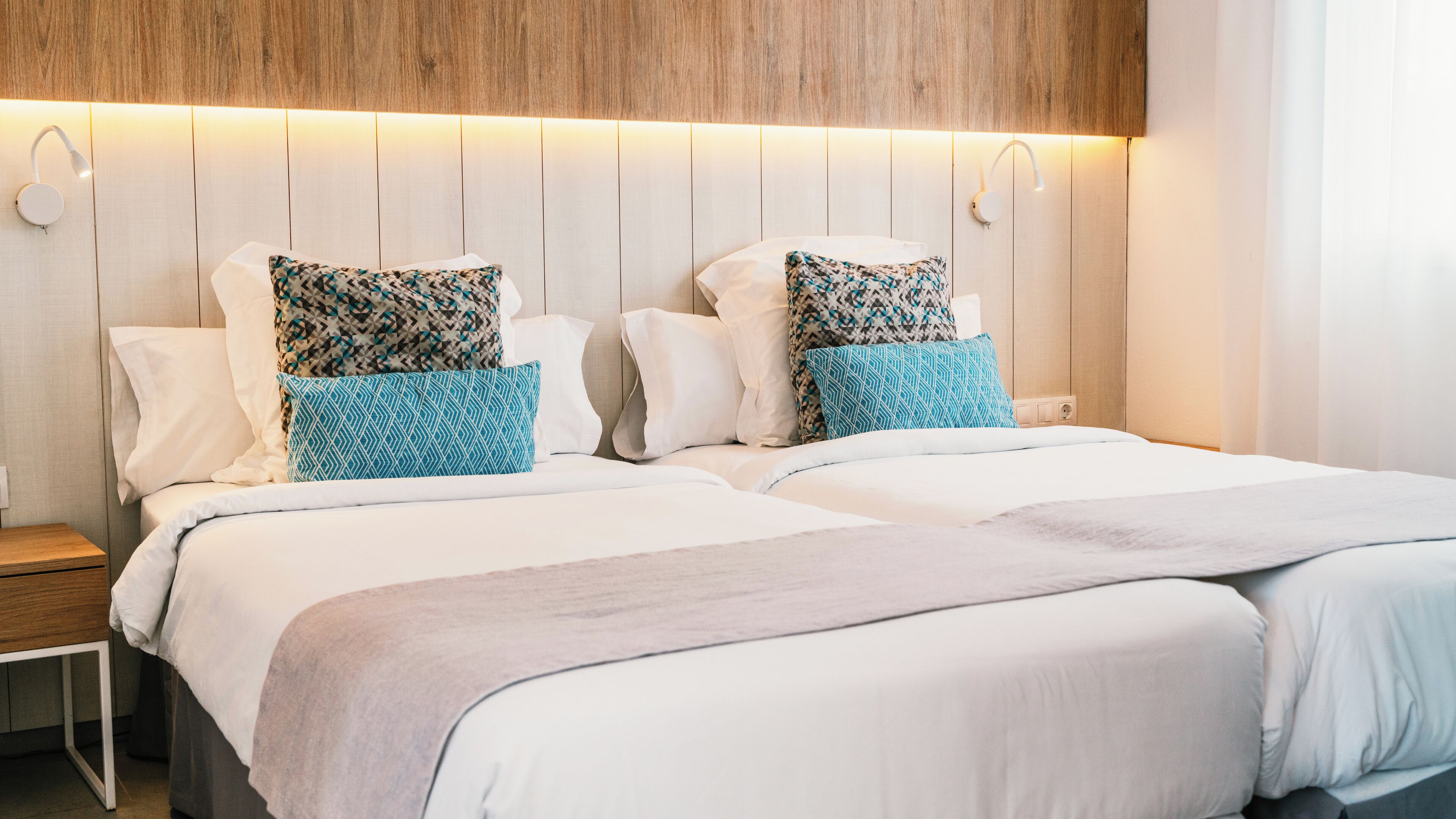 A double bed with patterned pillows, a bedside table, and a wooden headboard with integrated lighting.