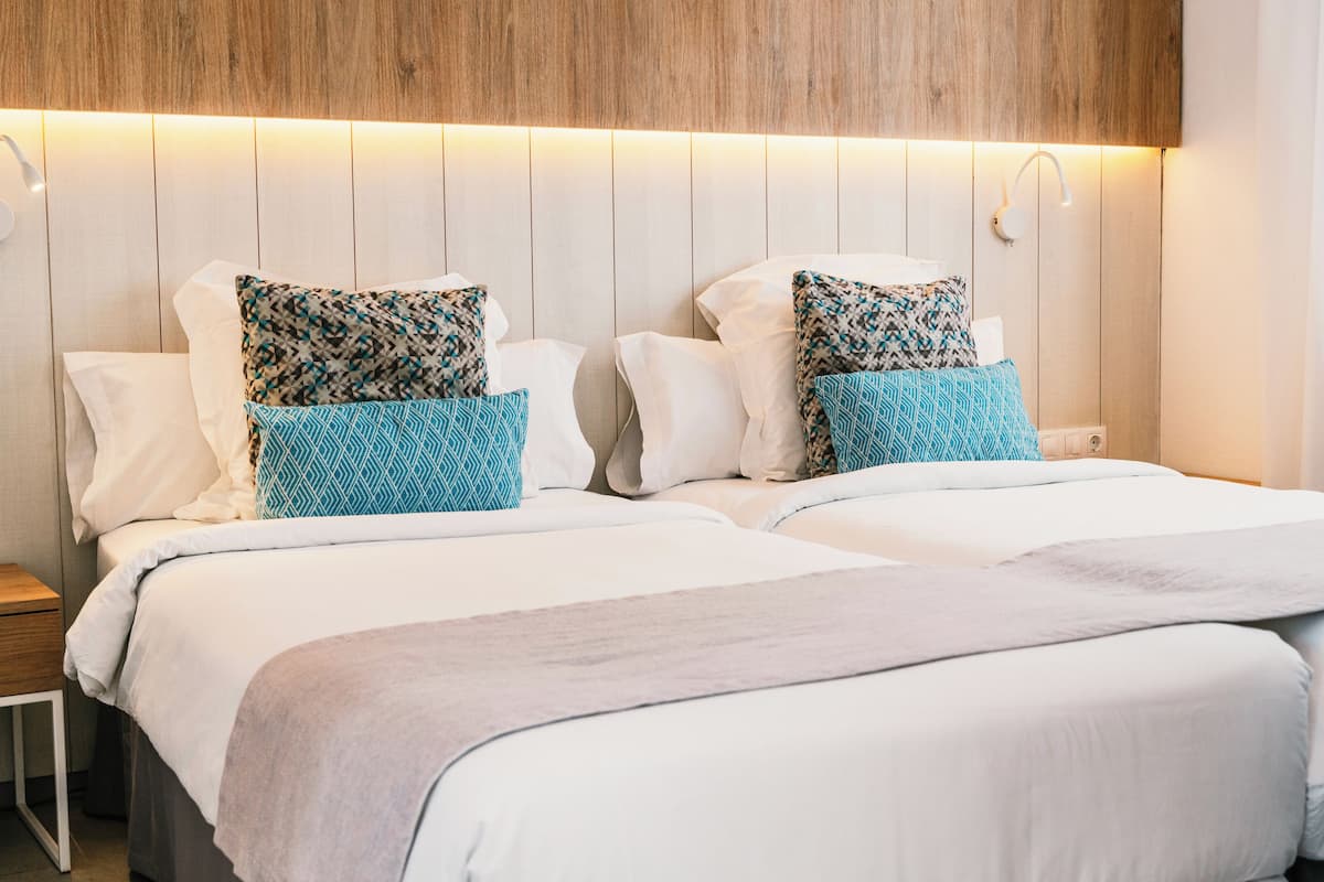 A double bed with patterned pillows, a bedside table, and a wooden headboard with integrated lighting.