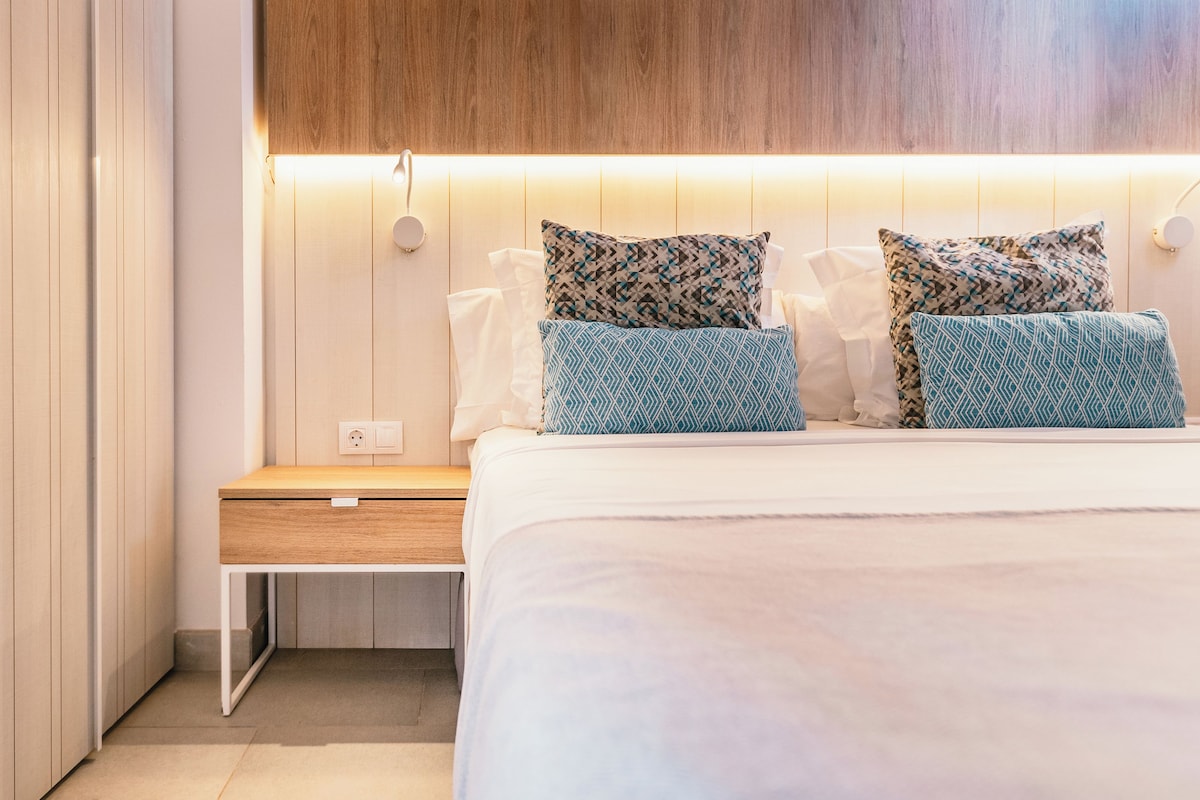 A modern bedroom with a wooden headboard, a bedside table, and a bed with patterned pillows.