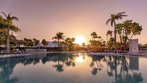 A resort pool with clear water reflecting the sunset, surrounded by palm trees and lounge chairs. - LABRANDA Alyssa Suite Hotel (Yaiza)