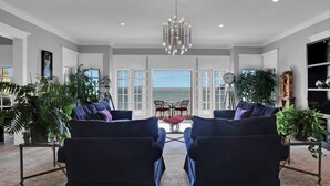 A spacious living room with a view of the ocean, featuring two dark armchairs, a chandelier, and several potted plants. - Somerset Bed and Breakfast (Niagara-on-the-Lake)