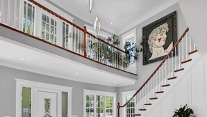 A spacious foyer with a grand staircase, a bench with patterned cushions, and a large framed artwork on the wall. - Somerset Bed and Breakfast (Niagara-on-the-Lake)