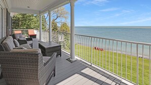 A covered porch with wicker furniture, a view of the water, and a white railing. - Somerset Bed and Breakfast (Niagara-on-the-Lake)