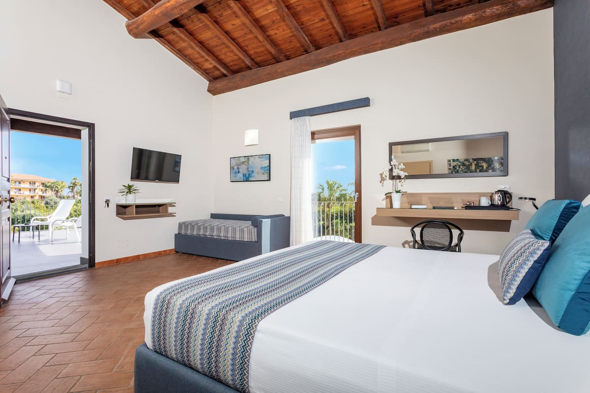 Ein Schlafzimmer mit einem großen Bett, einer Couch, einem Fernseher, einem Balkon und Blick auf ein Gebäude.