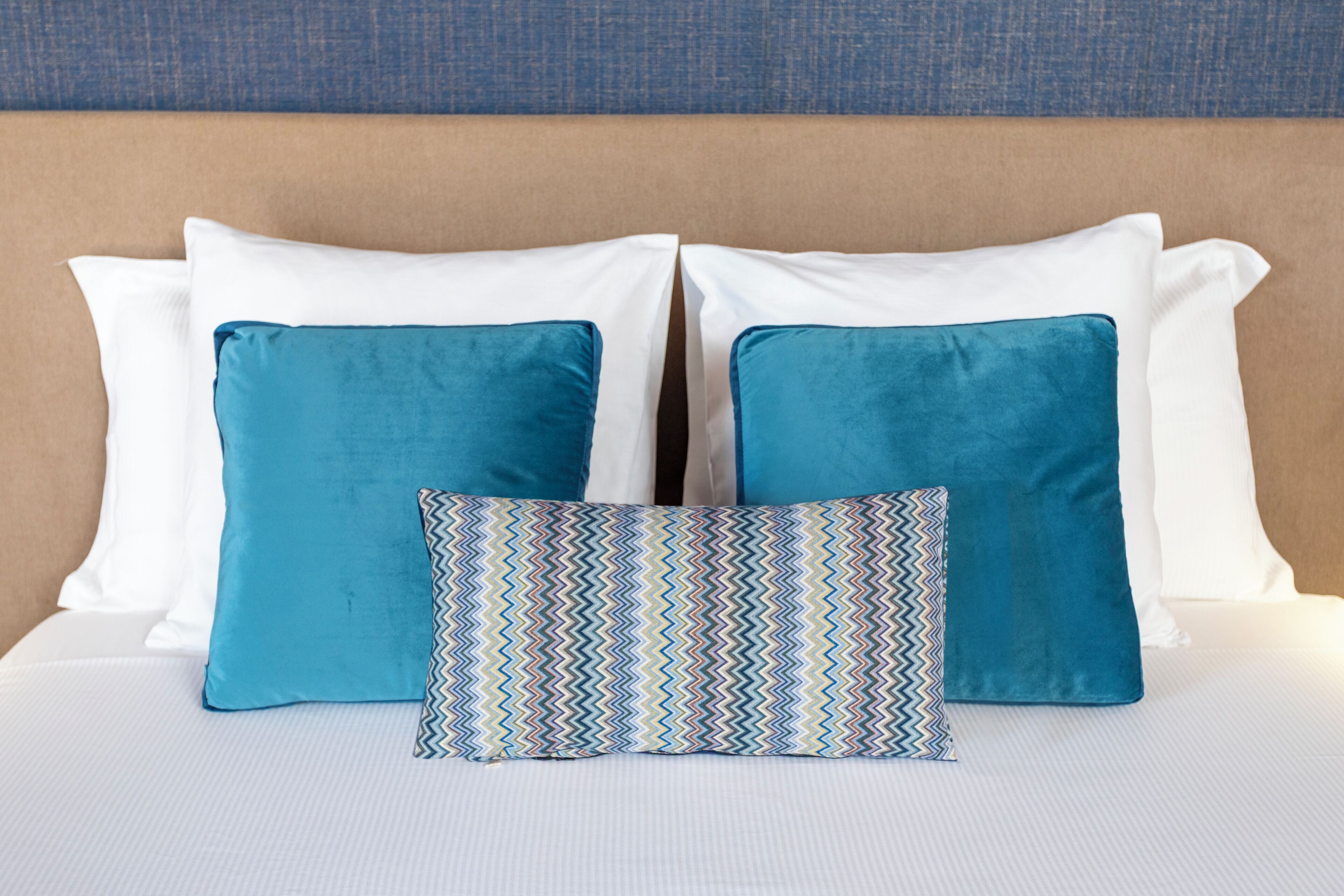 A bed with two white pillows and two blue pillows, and a patterned pillow in the center.