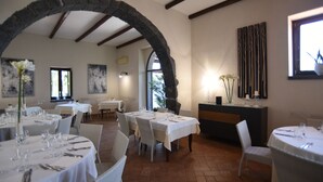 Un restaurant avec plusieurs tables dressées pour le service, une arche en pierre et une vue sur l’extérieur.
