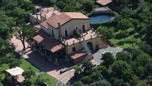 Un grand bâtiment à deux étages, doté d’un toit en tuiles, entouré d’une végétation luxuriante et agrémenté d’une petite piscine.