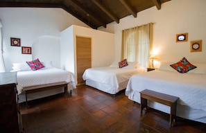 A room with two beds, a wooden bench, and a door. - Hotel Monasterio (Antigua Guatemala)