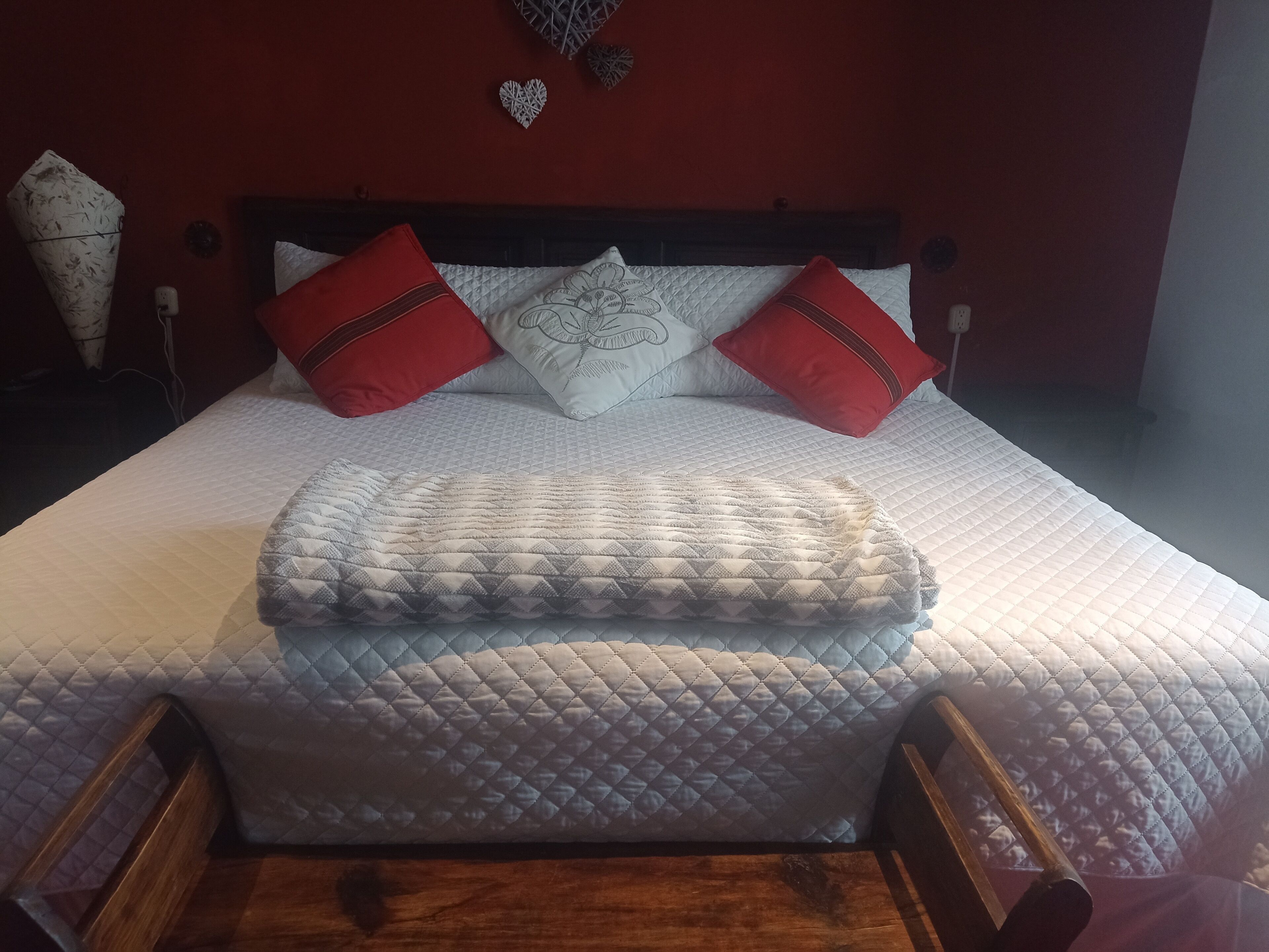 A neatly made bed with a quilted white duvet, two red pillows, and a decorative pillow with a floral design.