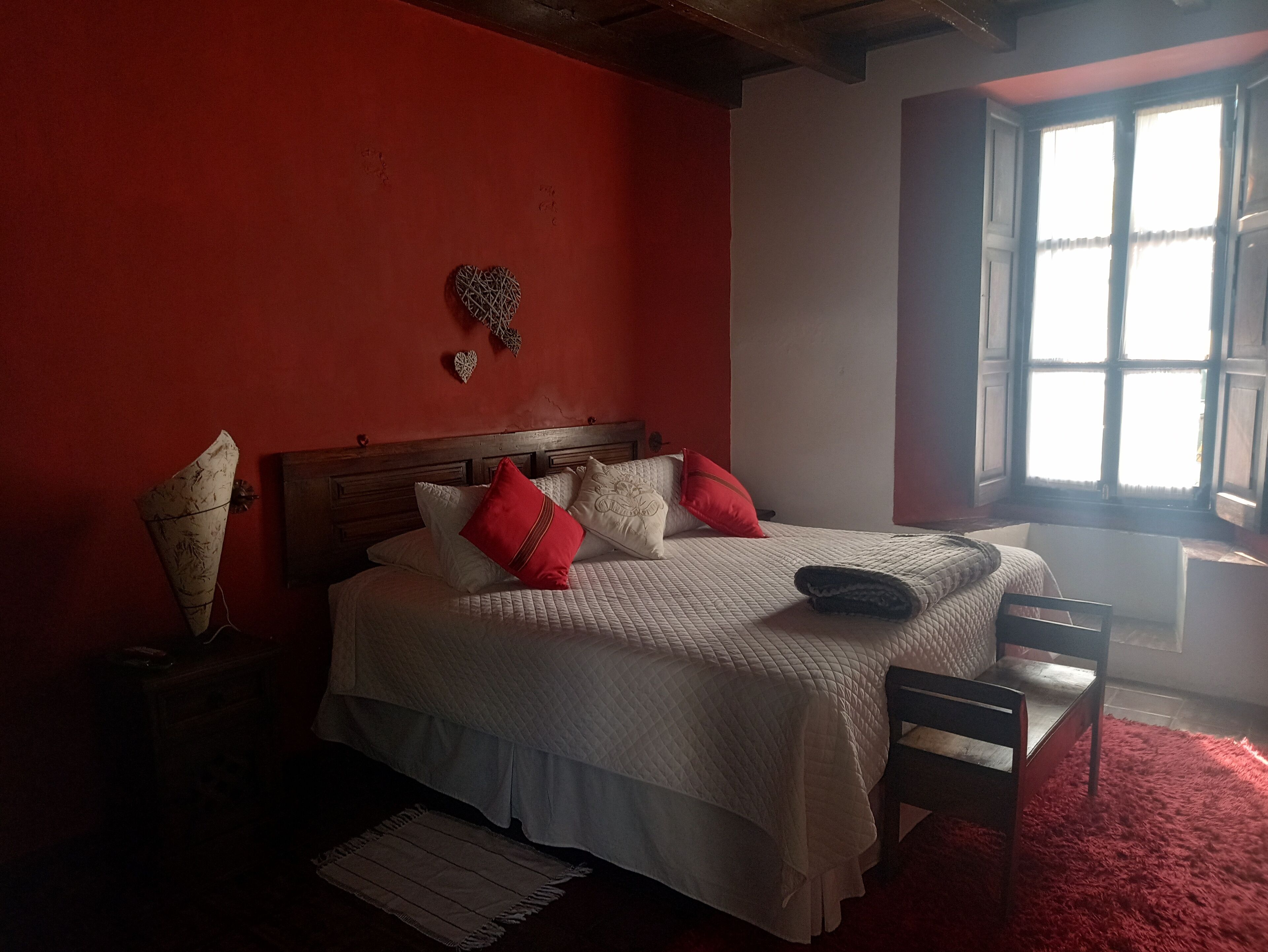 Ein Schlafzimmer mit einem Bett, Kissen, einem hölzernen Kopfteil, einem roten Teppich und einem Fenster mit Vorhängen.
