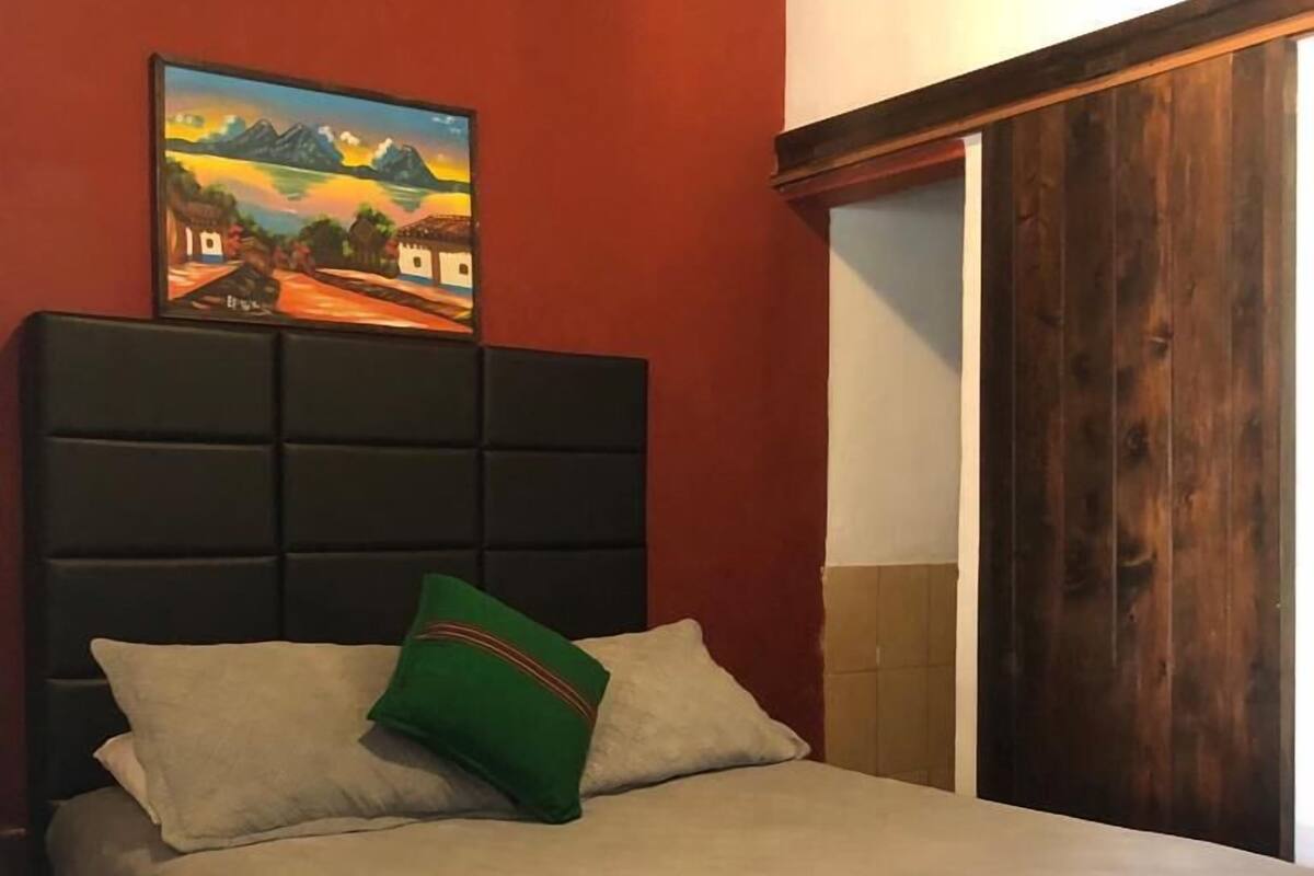 A bed with a headboard, a pillow, and a painting on the wall.