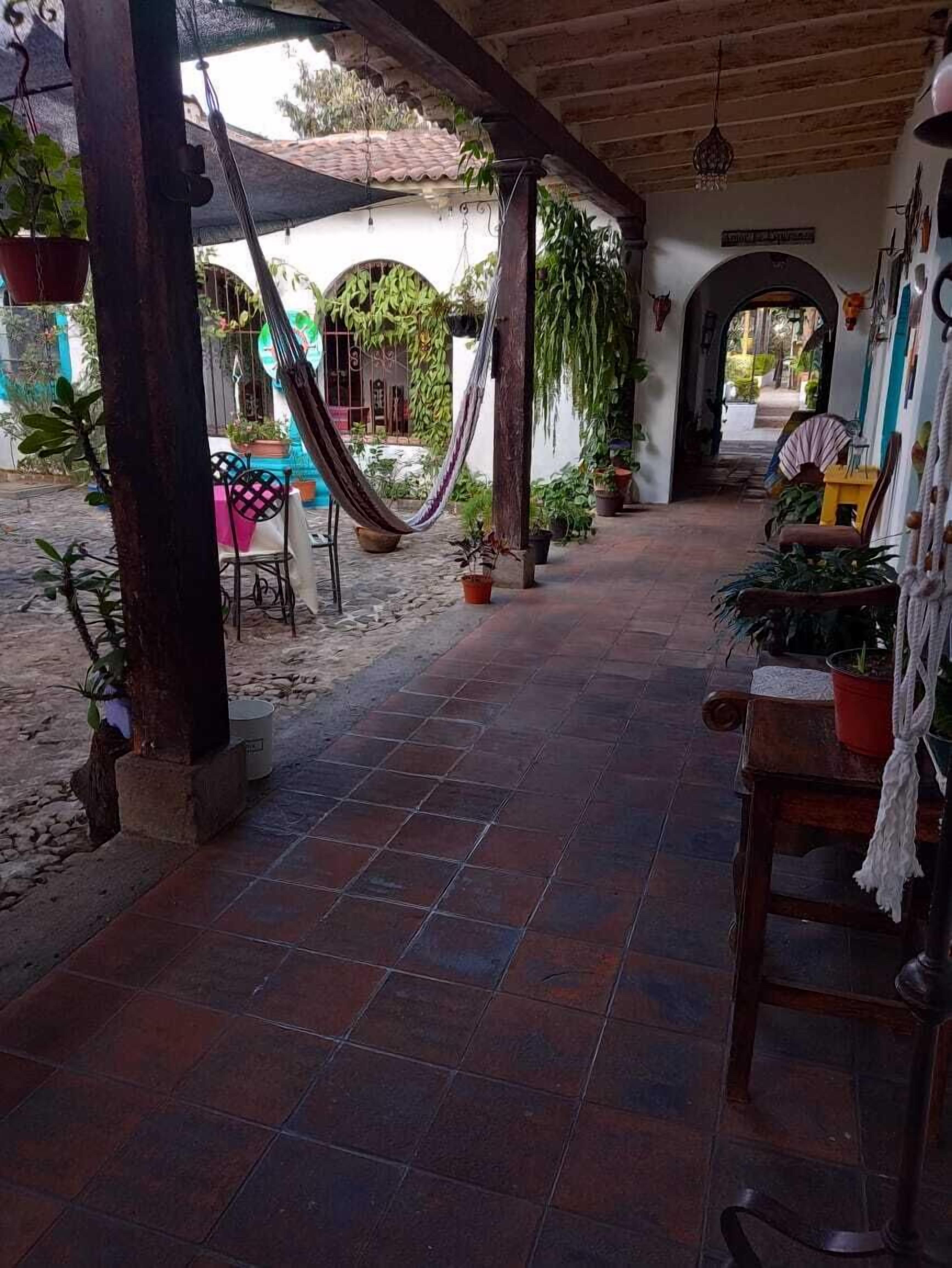 A covered outdoor area with a tiled floor, a hammock, and various potted plants.
