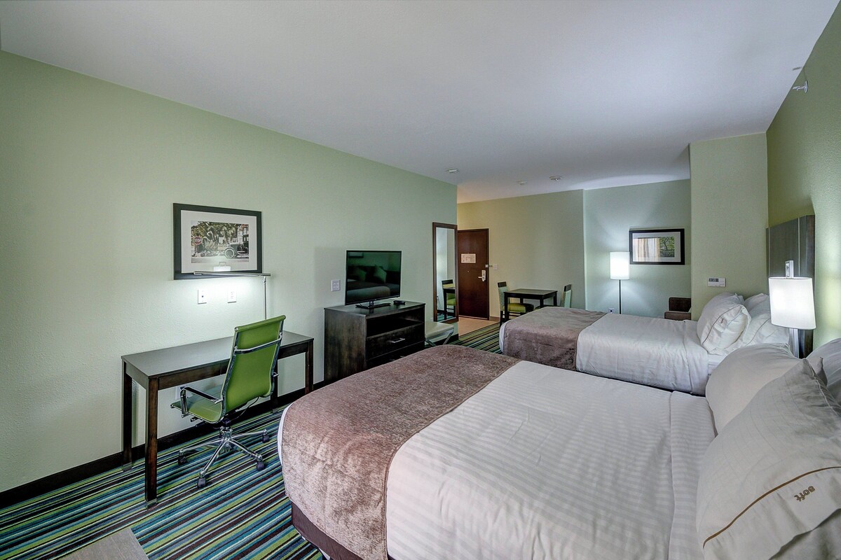 Une chambre d’hôtel avec deux lits, un bureau avec une chaise, une télévision et une porte donnant sur une autre pièce.