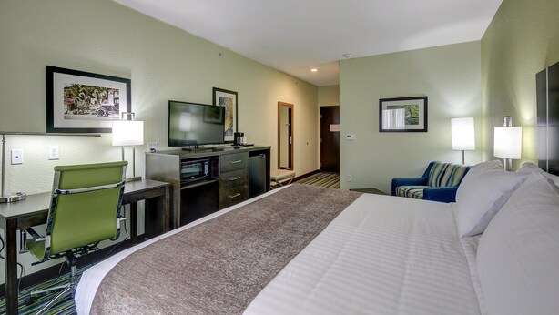 A hotel room with a large bed, a desk with a chair, a television, and a door leading to another room.