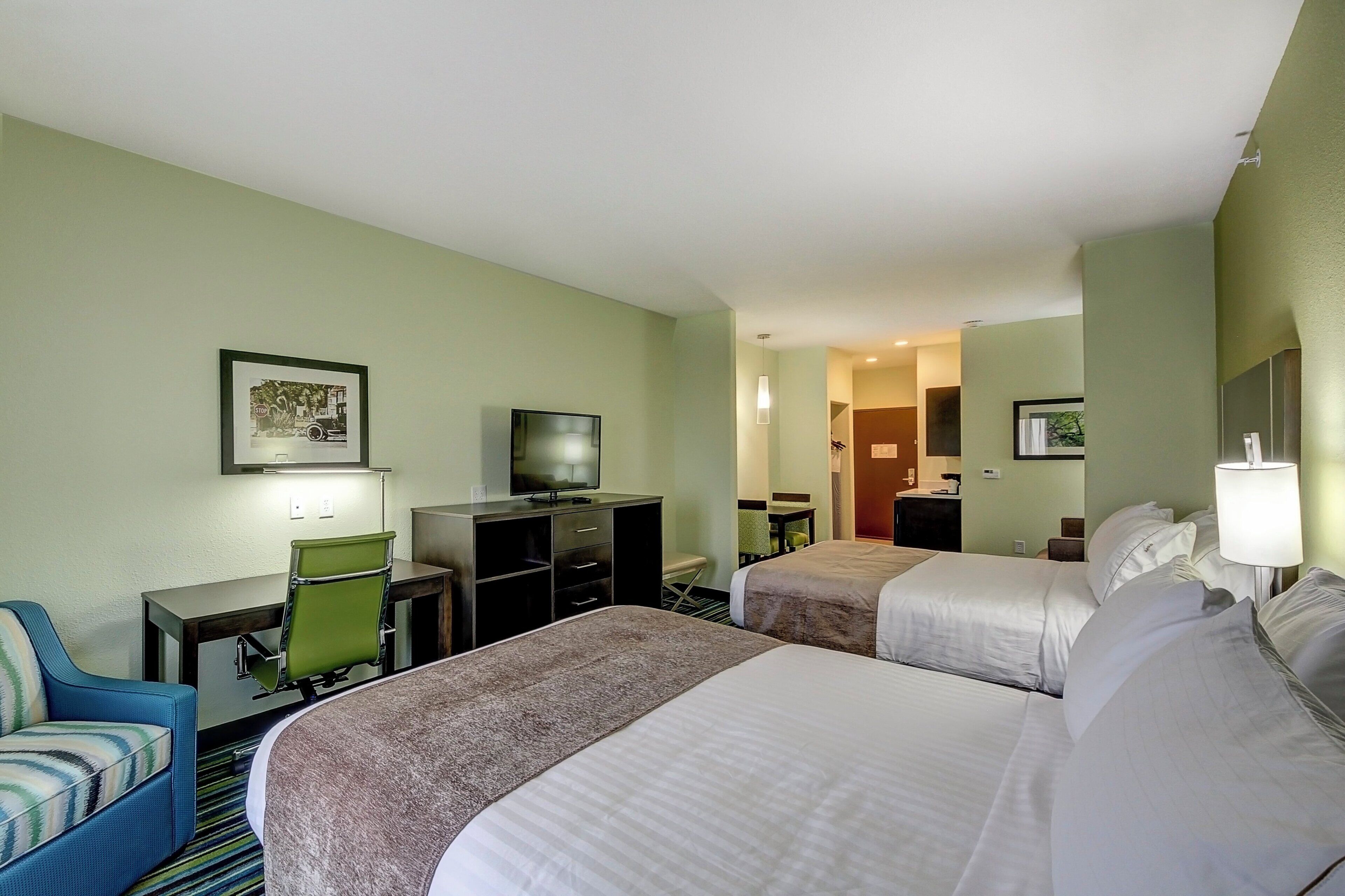 A hotel room with two beds, a desk with a television, a chair, and a small table.