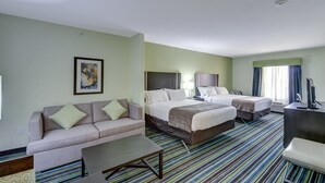 A hotel room with a sofa, two beds, a desk, and a striped carpet.