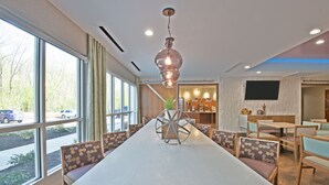 A modern conference room with a long table, comfortable seating, and large windows offering a view of the street.