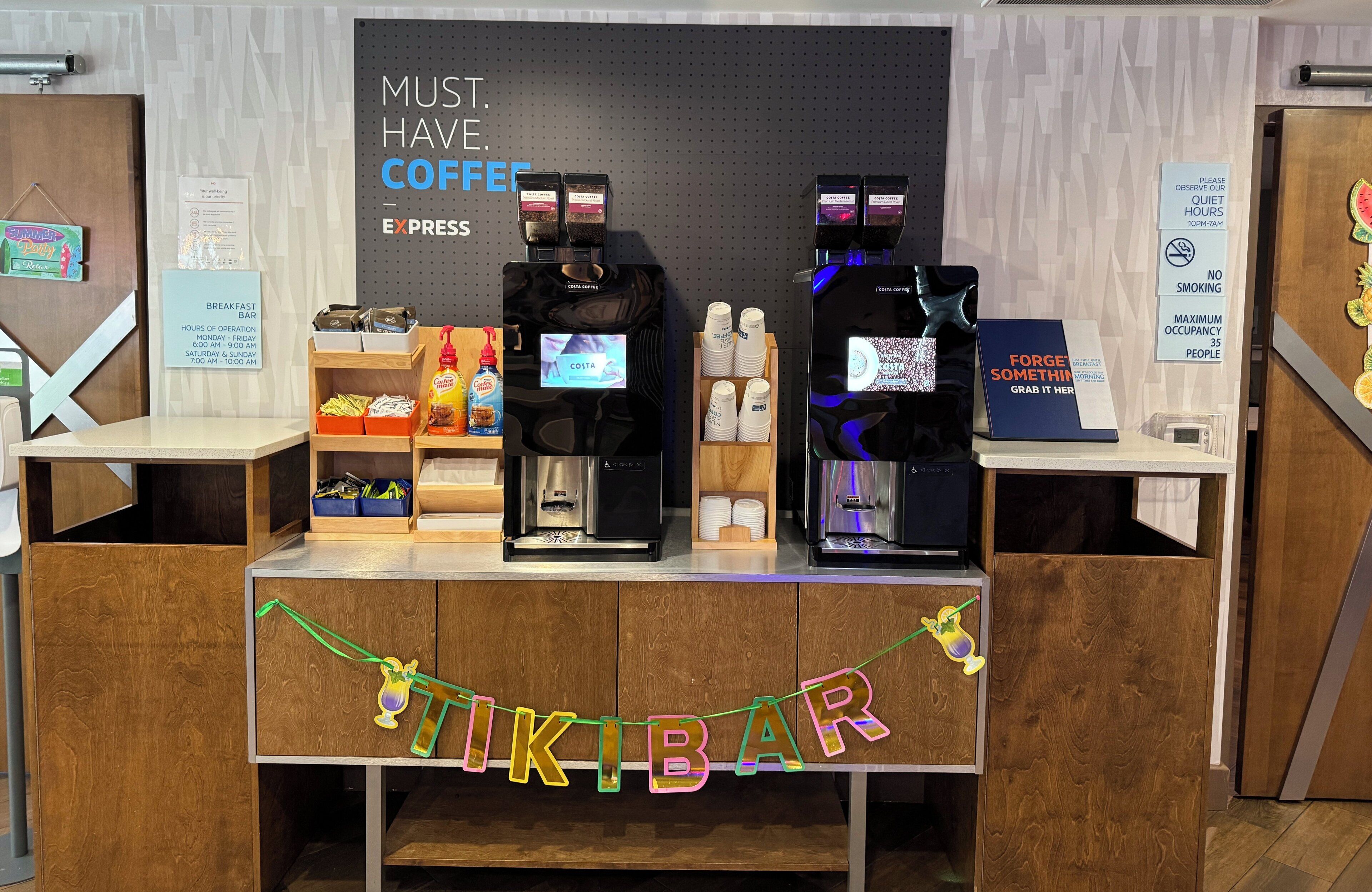 A coffee bar with two espresso machines, a sign reading "MUST. HAVE. COFFEE. EXPRESS.", and a "FORGE SOMETHING. GRAB IT HERE." sign.