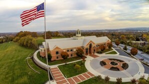 A large brick building with a central courtyard, surrounded by a well-maintained lawn and a flagpole with an American flag.