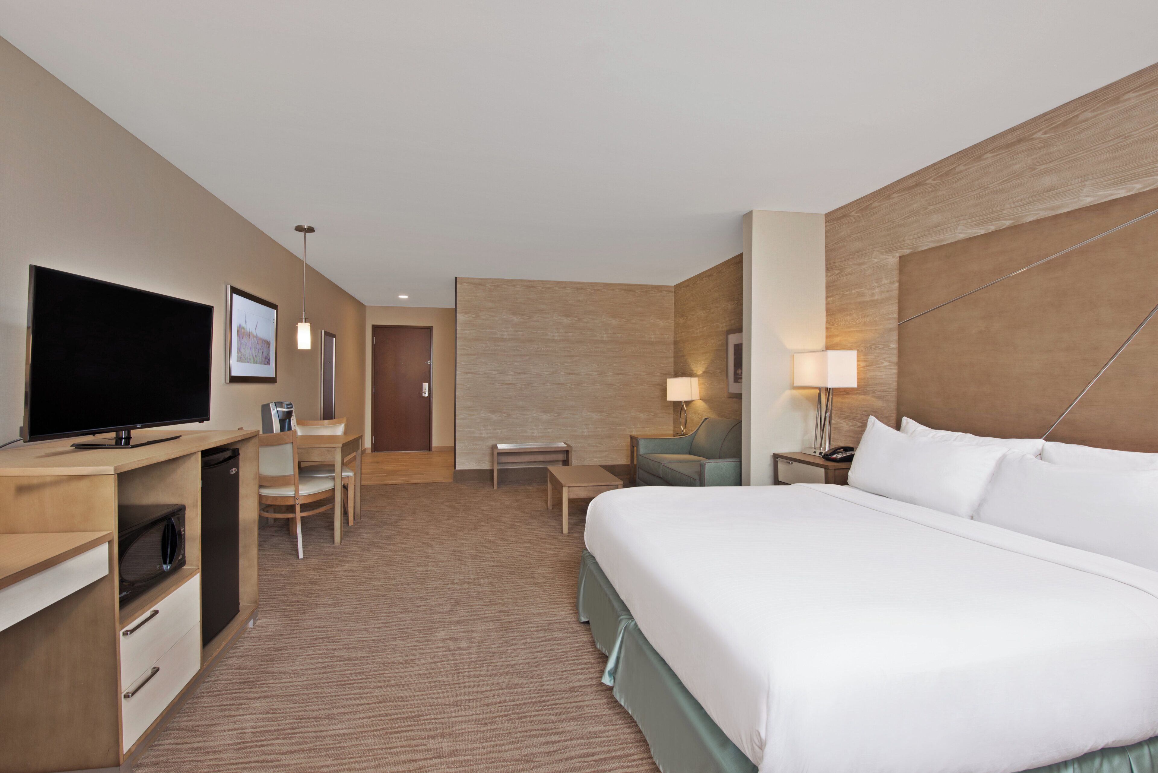 Habitación de hotel con cama, escritorio, silla, televisión y una mesita.