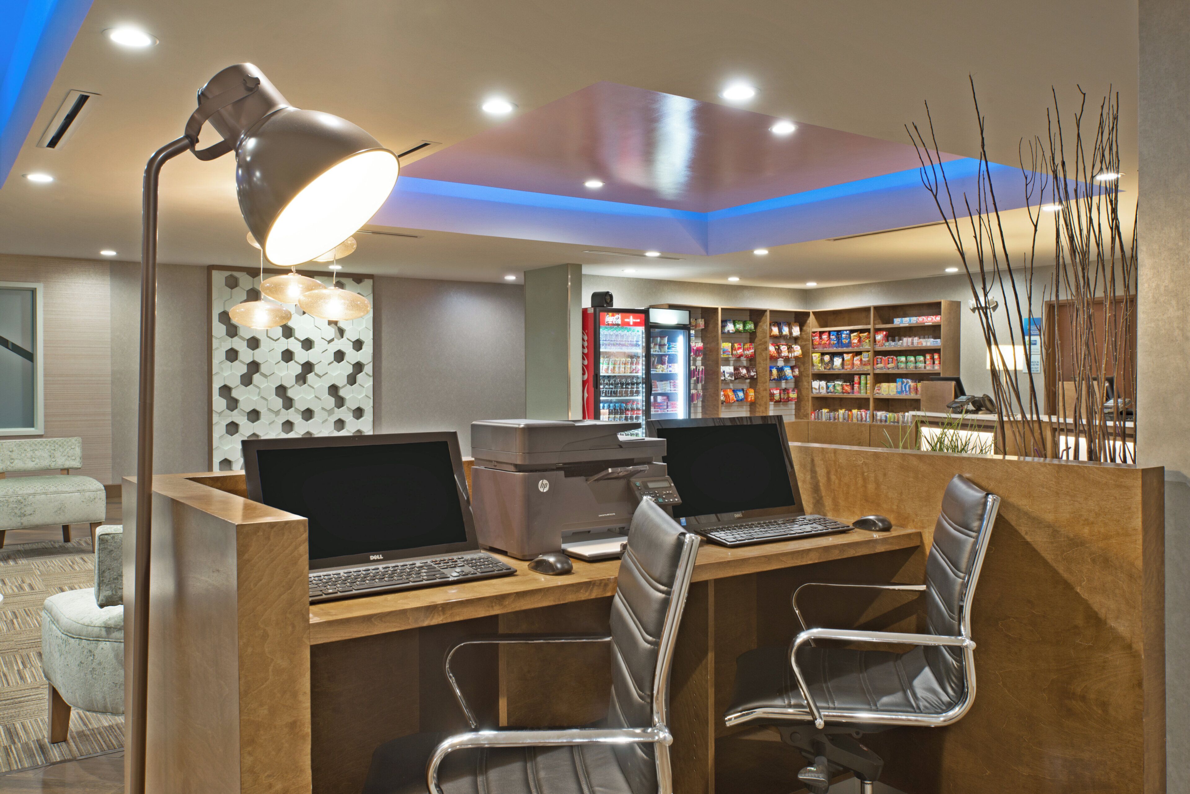 A hotel lobby with a reception desk, two computer workstations, a vending machine, and a seating area with a patterned wall.