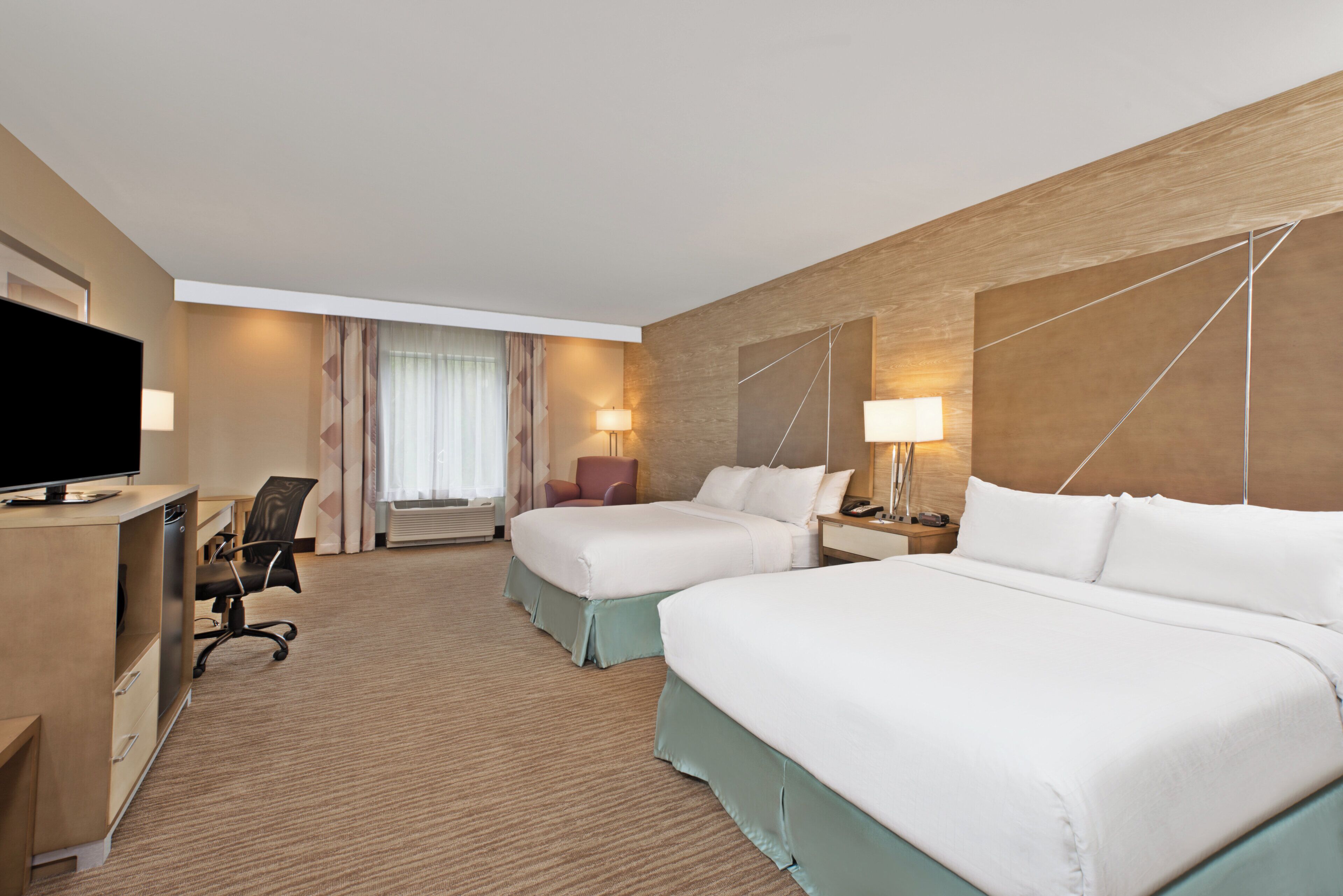 Une chambre d’hôtel avec deux lits, un bureau avec une télévision, une chaise et une fenêtre avec des rideaux.