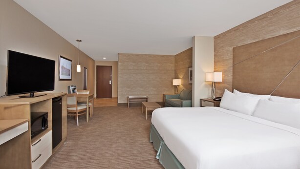 A hotel room with a large bed, a desk with a television, a chair, a small table, and a lamp.