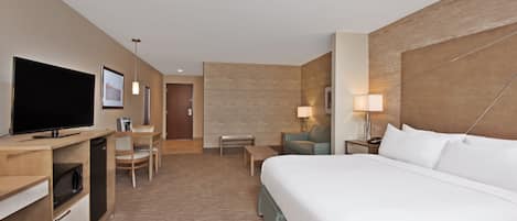Habitación de hotel con una cama grande, un escritorio con televisor, una silla, una mesita y una lámpara.