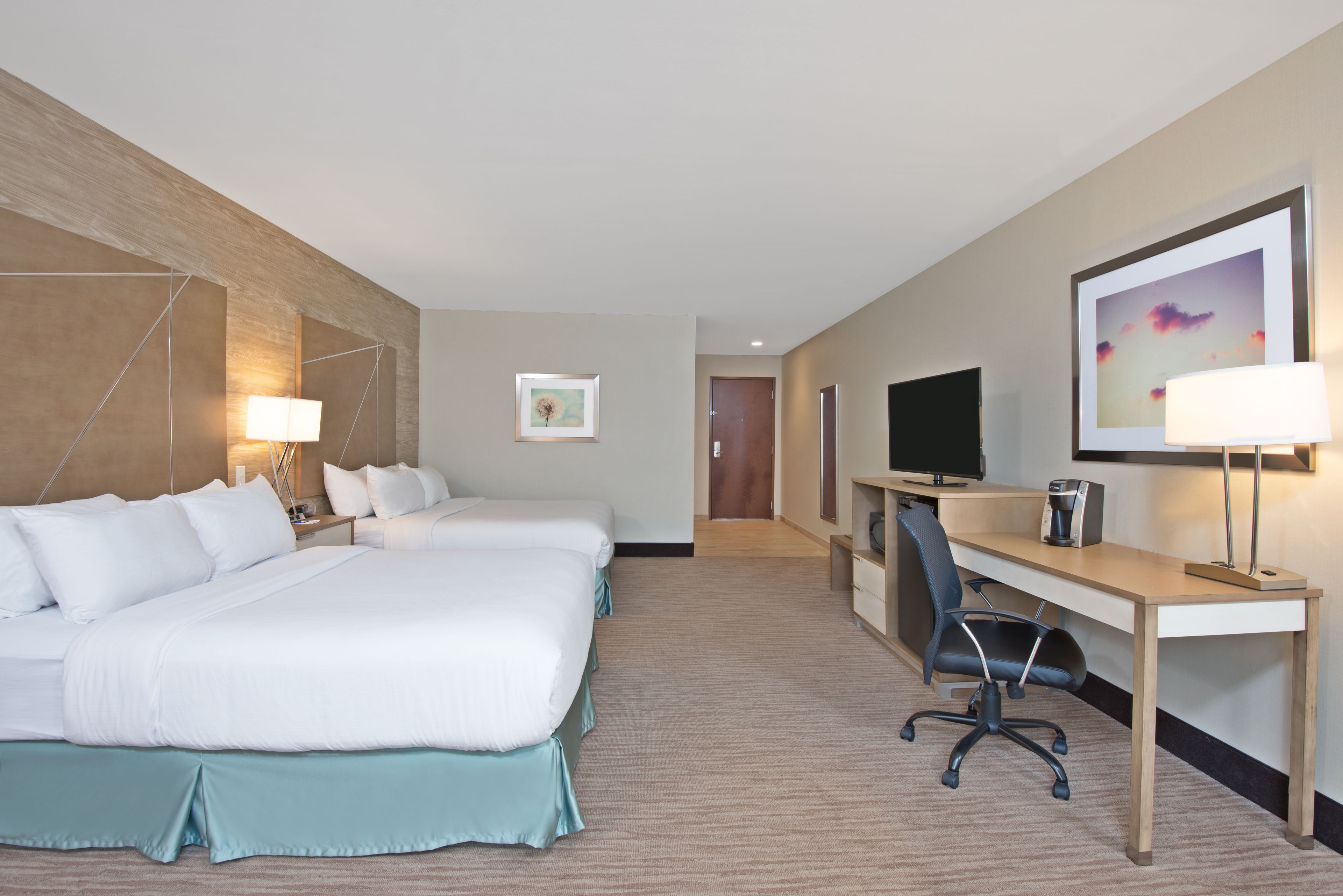 A hotel room with two beds, a desk, a chair, a television, and a framed picture on the wall.