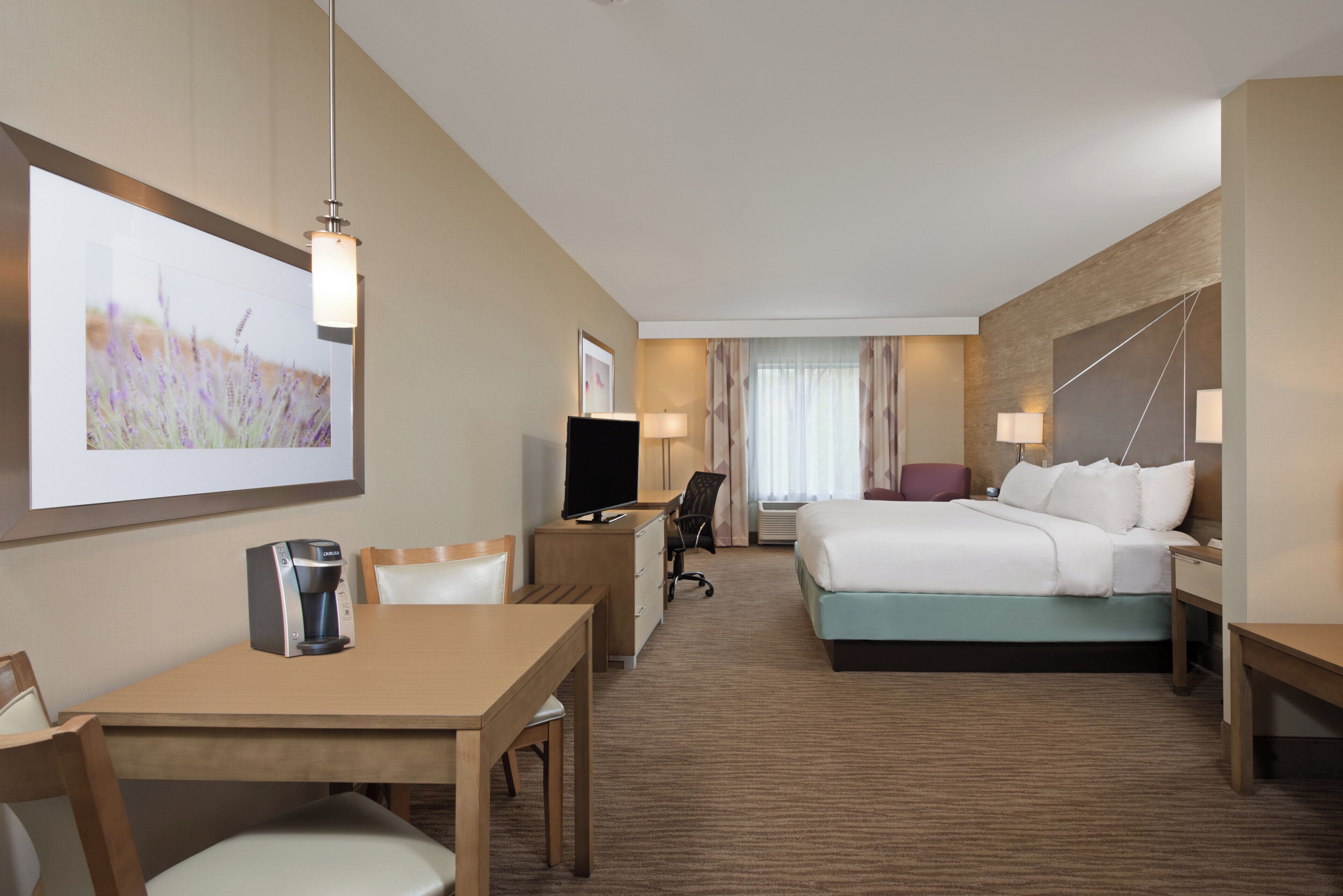 A hotel room with a bed, desk, chair, TV, and a coffee machine.