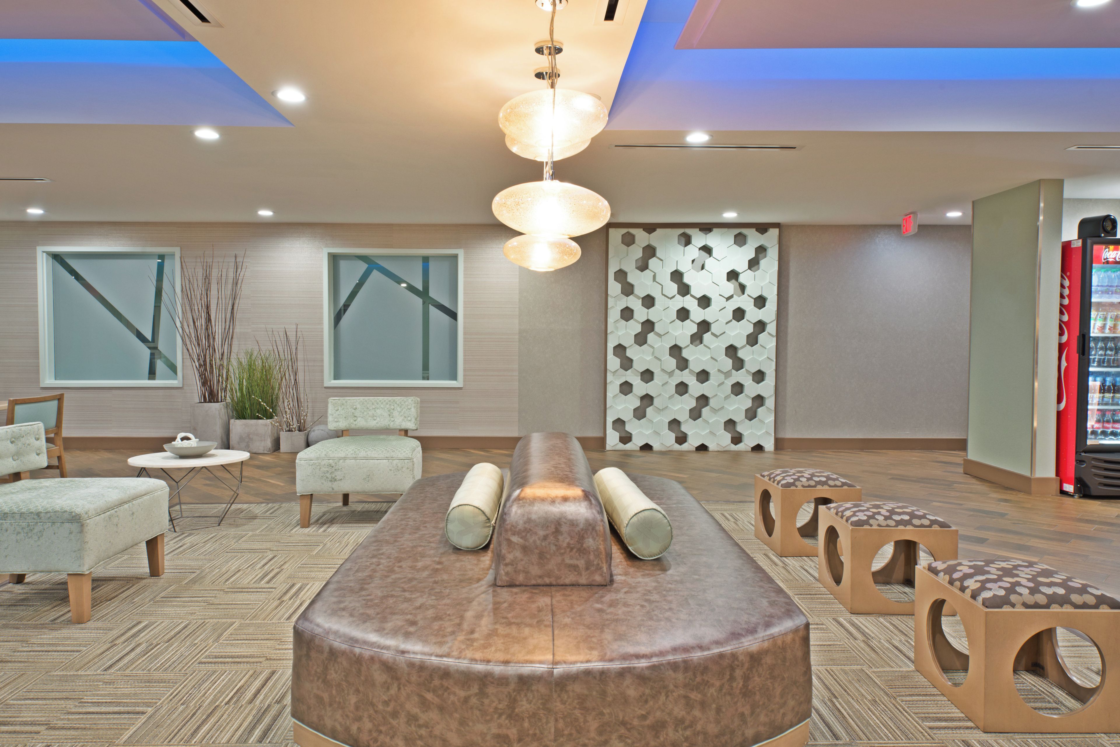A modern lounge area with a central seating arrangement, a decorative wall panel, and a vending machine.