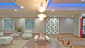 A modern waiting area with a central seating area, a patterned wall, and a vending machine. - Holiday Inn Express & Suites New Cumberland by IHG (New Cumberland)