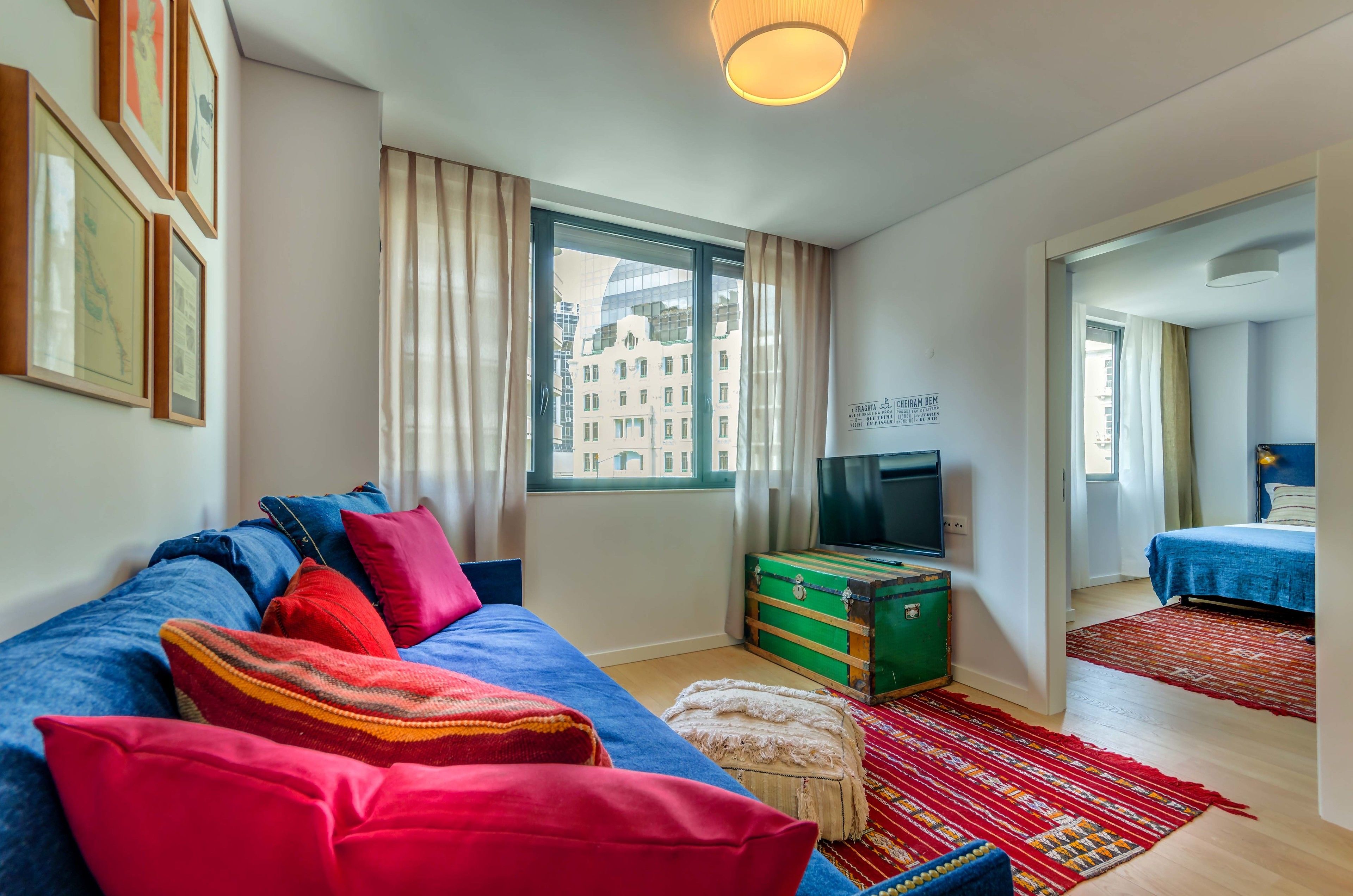 A modern hotel room with a large bed, a TV, a suitcase, and a view of the cityscape through the window.