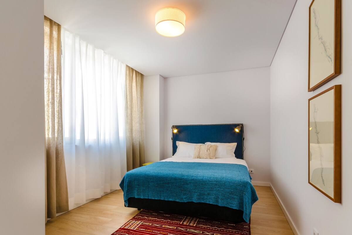 Een slaapkamer met een bed, een rood vloerkleed en een plafondlamp.
