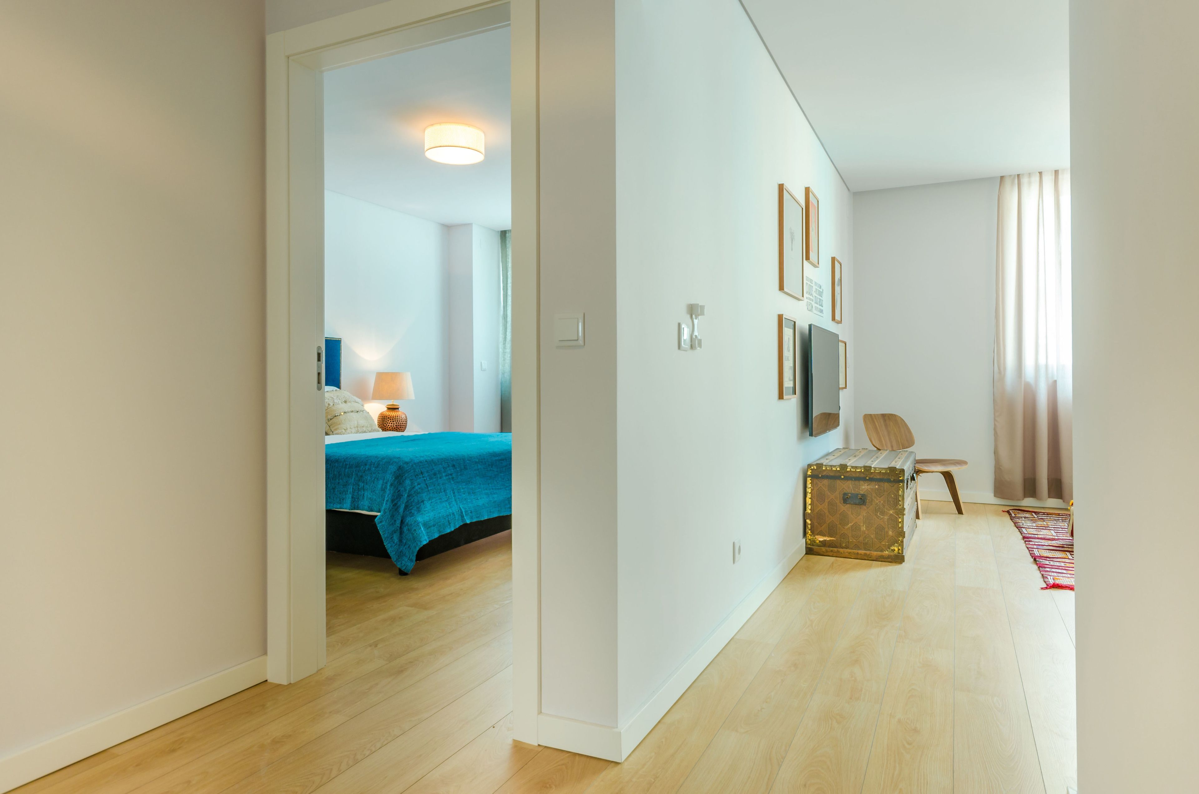 Habitación de hotel moderna con piso de madera, cama con cubierta azul, maleta y una silla.