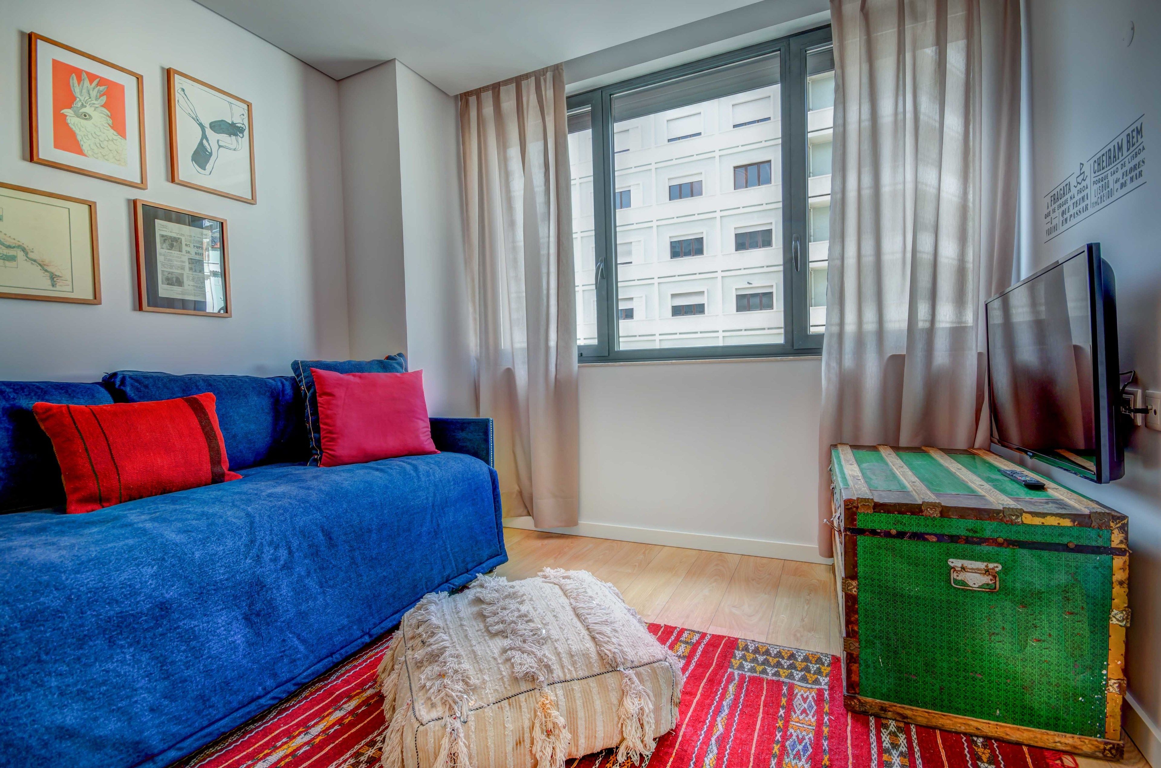 A room with a blue sofa, a green suitcase, and a window with curtains.
